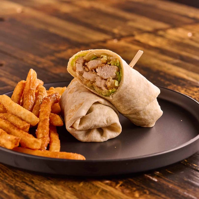 Chicken wrap cut in half, revealing chicken and lettuce, served with a side of golden french fries.
