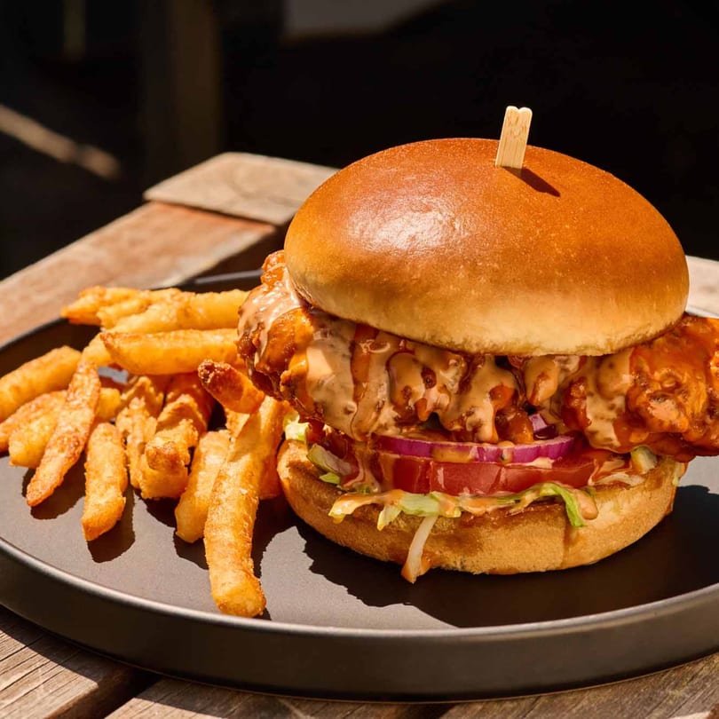 A crispy chicken sandwich with sauce, lettuce, tomato, and red onion, served with a side of fries.