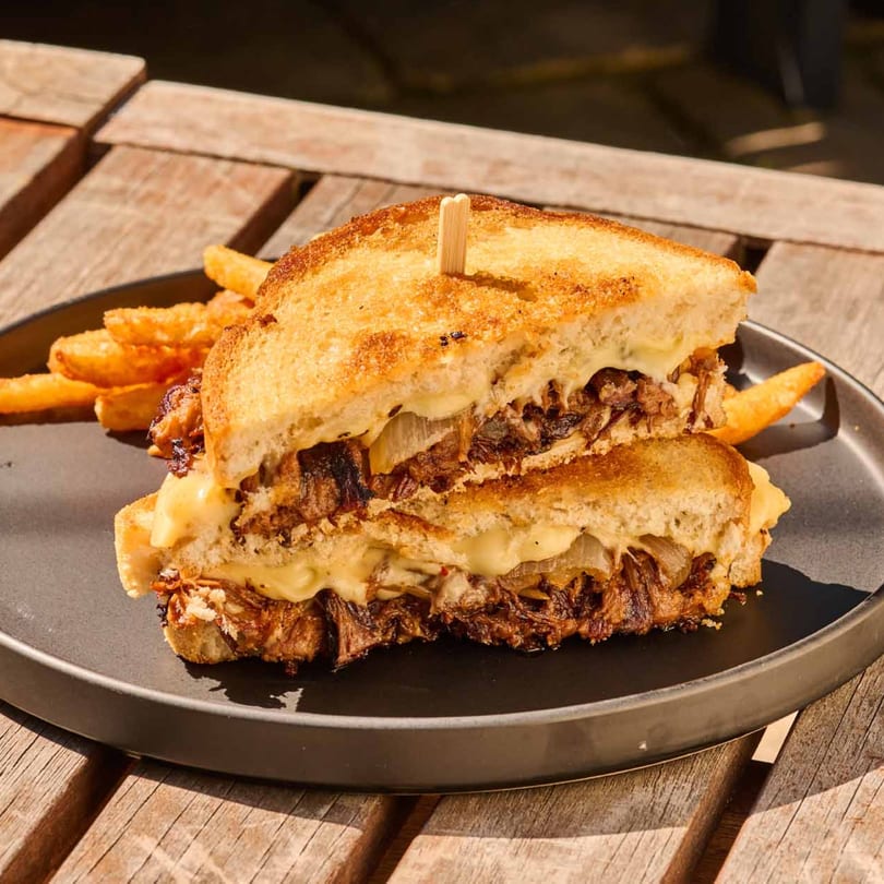 Grilled cheese sandwich with pulled pork and caramelized onions, served with fries on a black plate.